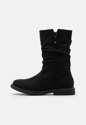 Botte noire mi-mollet avec une tige souple, un bout rond, un petit talon bas empilé et une petite languette décorative près de l'ouverture supérieure.