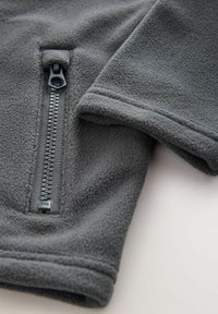 Grauer Fleece-Jacke mit Detail, das einen halben Reißverschluss vorne und eine glatte Textur aufweist, mit Bündchen und einem Reißverschlussverschluss an der Brust.