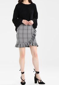 Svart stickad tröja med vida ärmar, kombinerad med en grå rutigt volangkjol. Svarta klacksandaler med ankelband fulländar looken.