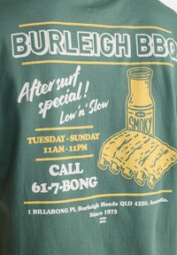Κείμενο σε μπλουζάκι Burleigh BBQ που προωθεί ειδικές προσφορές μετά το σερφ, καπνιστή σάλτσα, εικονογράφηση με παϊδάκια, ώρες λειτουργίας Τρίτη-Κυριακή 11 π.μ.-11 μ.μ. και στοιχεία επικοινωνίας στο Burleigh Heads.