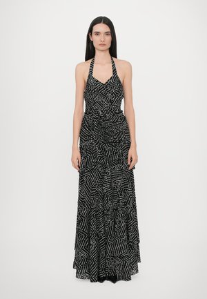 Zwarte halterjurk met een geometrisch wit patroon. Heeft een aansluitend lijfje, een geplisseerde taille en een gelaagde rok. Lichte stof.
