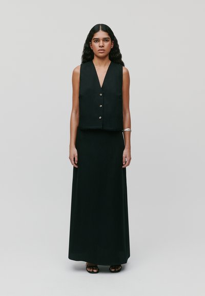 Gilet sans manches noir avec un décolleté en V et une fermeture par bouton, associé à une longue jupe noire fluide. Tissu lisse et design minimaliste.