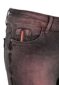 Jean en denim avec un dégradé noir et rouge délavé, comportant une petite poche zippée avec des accents rouges et des coutures contrastées.