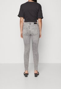Jeans de denim gris ajustados con una cintura de altura media, diseño clásico de cinco bolsillos y una textura suave, combinados con una blusa negra de manga corta.