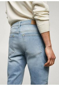 Vaaleansiniset farkut kapealla istuvuudella, joissa on nahkainen merkki vyötäröllä ja ommellut taskut klassisella designilla.