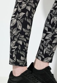 Zwarte leggings met witte bladerenpatronen, met een aansluitend ontwerp en een gladde textuur, gecombineerd met zwarte suède sneakers.