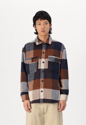 Plaid flannel shirt featuring brown, navy, and beige colors, two front pockets, and a button-up design with a classic collar.