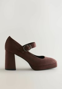 Pantof suede maro cu toc înalt, vârf rotund, curea la gleznă și cataramă circulară. Dispune de un toc voluminos și o platformă pentru înălțime suplimentară.
