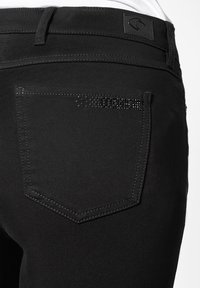 Zwarte jeans met een achterzak voorzien van een decoratieve lijn van kleine zwarte studs, afgewerkt met contrasterende stiksels en een merklabel op de taille.