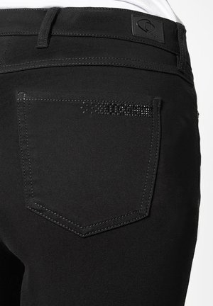 Czarne dżinsy z tylną kieszenią ozdobioną dekoracyjną linią małych czarnych ćwieków, wykończone kontrastowym przeszyciem i metką markową w pasie.