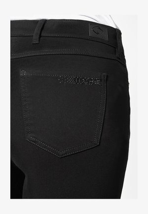 Sorte jeans med en baglomme prydet med en dekorativ række små sorte nitter, afsluttet med kontrasterende syninger og et mærke på taljen.