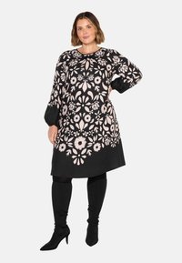 Mustapuku, jossa on monimutkaisia vaaleanpunaisia kukkakuvioita, pitkät hihat, pyöreä pääntie ja rento istuvuus; yhdistetty polven yli ulottuviin mustiin saappaisiin.