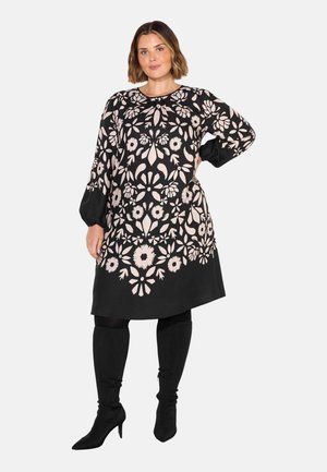 Robe noire avec des motifs floraux roses complexes, manches longues, encolure arrondie et coupe décontractée ; associée à des bottes noires montantes.