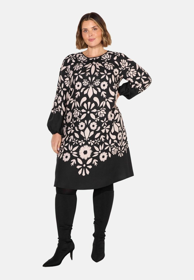 Mustapuku, jossa on monimutkaisia vaaleanpunaisia kukkakuvioita, pitkät hihat, pyöreä pääntie ja rento istuvuus; yhdistetty polven yli ulottuviin mustiin saappaisiin.