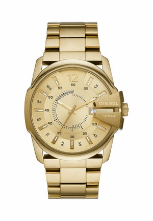 Reloj de pulsera Diesel dorado con correa de eslabones de metal, esfera redonda, ventana de fecha y protector de corona prominente en el lado derecho.