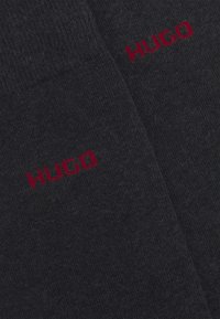 Dunkelgraue Socken mit einer weichen Textur und einem eingewebten roten "HUGO"-Logo. Einfaches Design mit nahtlosem Look und mittellanger Länge.