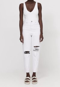 Jeans de mezclilla blanca de cintura alta con detalles desgastados en las rodillas, combinados con una camiseta sin mangas blanca y sandalias de color claro.