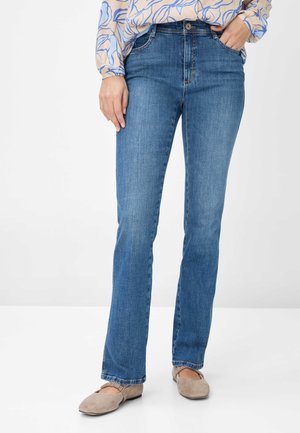 Blaue Denim-Jeans mit geradem Bein, ausgestattet mit fünf Taschen und einem Knopfverschluss, kombiniert mit beigen flachen Schuhen.