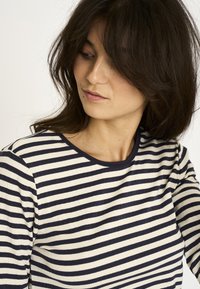 Langærmet top med marineblå og cremefarvede vandrette striber, ribbet tekstur og en kontrastfuld halsudskæring. Let tætsiddende design.