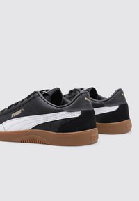 Sneaker bianche e nere con finitura in pelle liscia, dettagli in suede e suola in gomma; presentano un marchio dorato sul tallone.