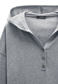 Szara koszulka henley z miękkiego materiału, z dużym kapturem, trzema guzikami z przodu oraz żebrowanym wykończeniem na dekolcie i mankietach.