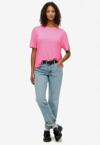 Lyserød kortærmet T-shirt i afslappet pasform, parret med lyseblå denimjeans, opsmøgede ved anklerne, suppleret med sorte sko og et bælte.