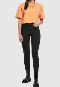 Oranžové zkrácené tričko s krátkými rukávy, kombinované s černými skinny džíny s vysokým pasem a chunky černými kotníkovými botami.