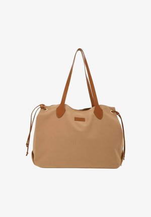 Sac fourre-tout beige avec des poignées en cuir marron et des cordons latéraux, avec un patch en cuir rectangulaire à l'avant.