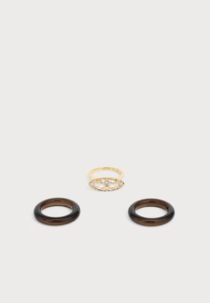 Drei Ringe auf einer hellen Oberfläche: ein goldener Ring mit einem großen ovalen klaren Stein, flankiert von kleinen Steinen, und zwei schlichte dunkelbraune runde Ringe.