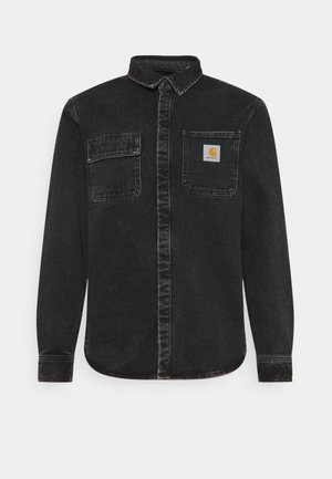 Schwarzes langärmeliges Jeanshemd mit Knöpfen und zwei Brusttaschen, eine davon mit einem kleinen gelben Carhartt-Logo-Aufnäher.