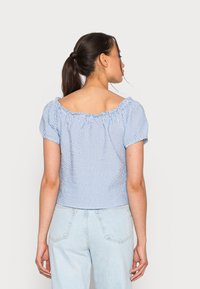 Blusão azul e branco às riscas com mangas curtas, decote elástico e tecido texturizado. Usado com jeans de cintura alta em azul claro.