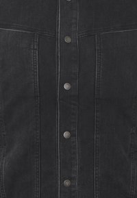 Svart denimjacka med knäppning framtill, prydd med silverfärgade metallknappar, strukturerade sömmar och två bröstfickor.