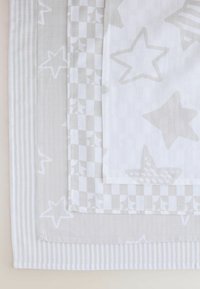 Grå og hvide tekstiler lagdelt, med stjernemønstre, ternede designs og stribede teksturer. Varierede stofoverflader og bløde udseender.