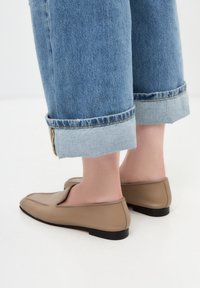 Loafers din piele bej cu vârf rotund, toc mic negru și cusături vizibile, purtați cu blugi de denim deschis albastru, croiți.