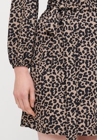 Leopardmønstret kjole i beige og sort med lange pufærmer, en tiestrømpe i taljen og tekstureret stof med en krøllet mønster.