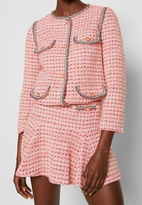 Conjunto de dos piezas que incluye una chaqueta de tweed texturizado rosa y blanca con ribetes negros y una minifalda acampanada a juego. Con bolsillos destacados.