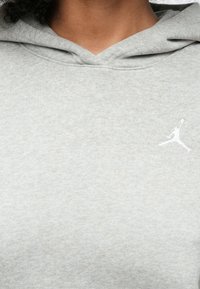 Hallikas pullover-tüüpi kapuutsiga dressipluus koos kengurutaskuga, millel on nööriga kapuuts ja vasakul rinnal valge Jumpman'i logo. Pehme kanga tekstuur.