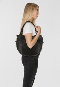 Borsa a spalla in pelle nera con forma curva, dotata di una tasca frontale e di un logo ancore in evidenza. La tracolla è regolabile e robusta.