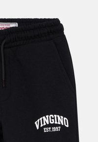 Čierne tepláky s elastickým pásom, bočnou kapsou a bielym potlačeným textom "VINGINO EST.1997" na stehne.