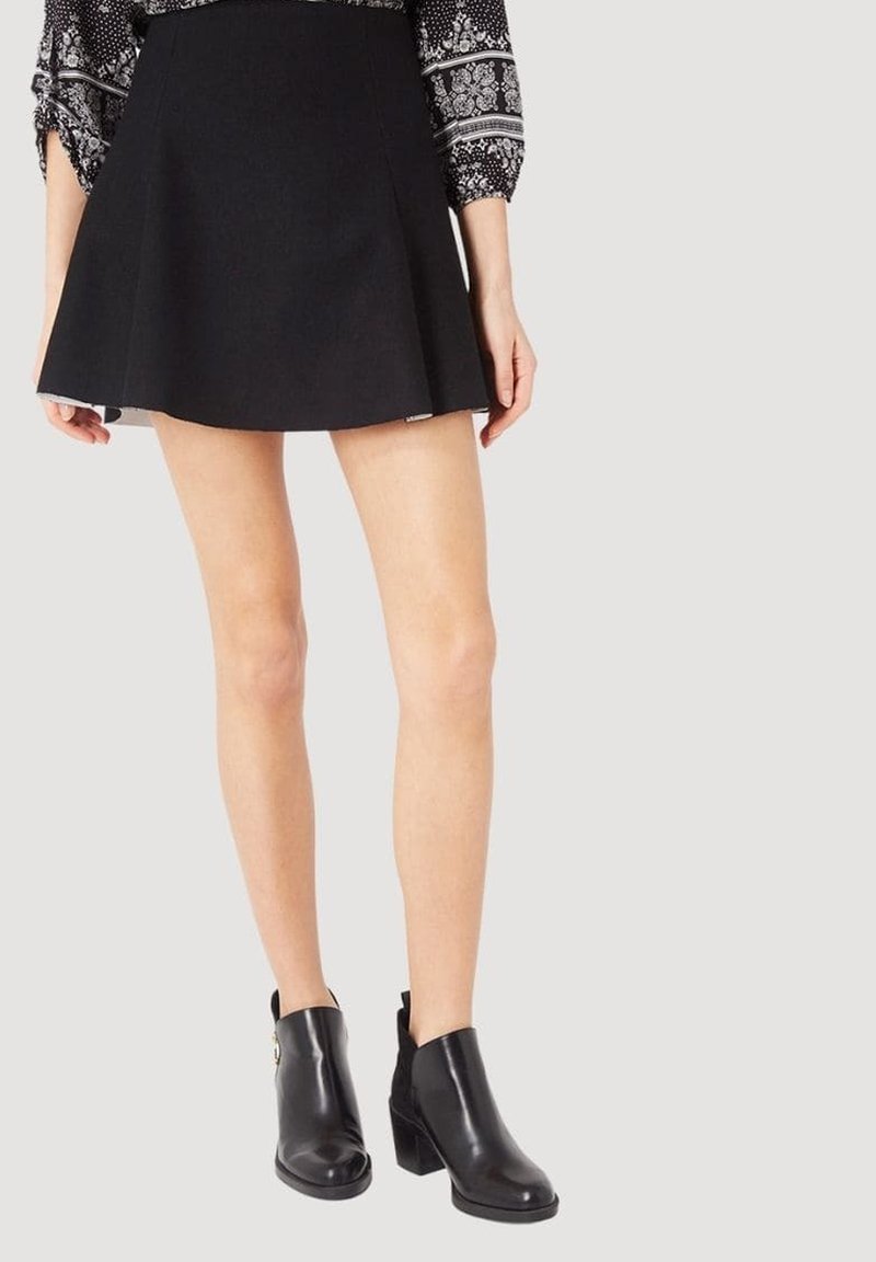 Falda negra acampanada con una textura suave, combinada con botines negros que tienen un acabado brillante y tacones gruesos.