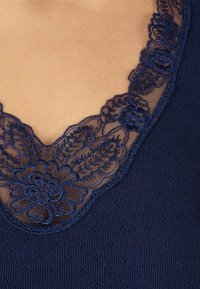 Top blu navy con scollo in pizzo floreale. Il tessuto è a costine, con un motivo testurizzato, e presenta dettagli in pizzo intricati sul colletto.