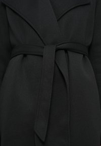 Μαύρο παλτό με σχέδιο τύπου wrap και ζώνη που δένει, κατασκευασμένο από μαλακό ύφασμα. Γιακάς φαρδύς, με απαλό, υφασμάτινο φινίρισμα.