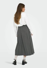 Falda midi plisada gris con cintura alta, combinada con una camisa blanca de botones y zapatos de tacón negros. Medias con encaje a la vista.