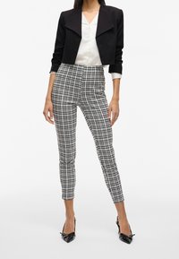 Svart kort jacka över en vit blus, parat med rutiga high waist byxor i svart och vitt, samt svarta spetsiga klackskor.