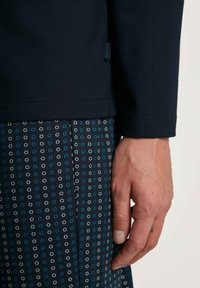 Chemise à manches longues marine avec une finition texturée, associée à un pantalon à motifs présentant des cercles concentriques blancs et bleus sur un fond sombre.