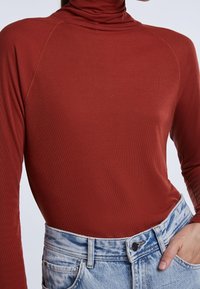 Collo caldo color ruggine realizzato in tessuto a coste, con maniche lunghe e design aderente, abbinato a pantaloni corti in denim a vita alta.