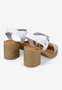 Sandalias de cuero blanco con un tacón de bloque de textura tejida y tira en el tobillo, que cuentan con una plantilla de imitación de cuero marrón y costuras decorativas en blanco.