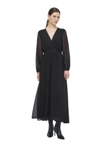 Abito lungo nero con scollo a V, maniche lunghe trasparenti e vita aderente. Texture liscia con orlo fluido, abbinato a stivali neri con tacco.