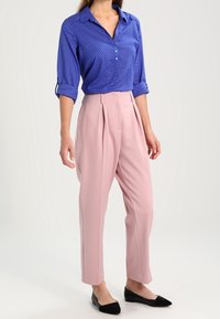 Camicia blu a pois con bottoni frontali, maniche arrotolate; abbinata a pantaloni rosa a vita alta e scarpe ballerine nere.