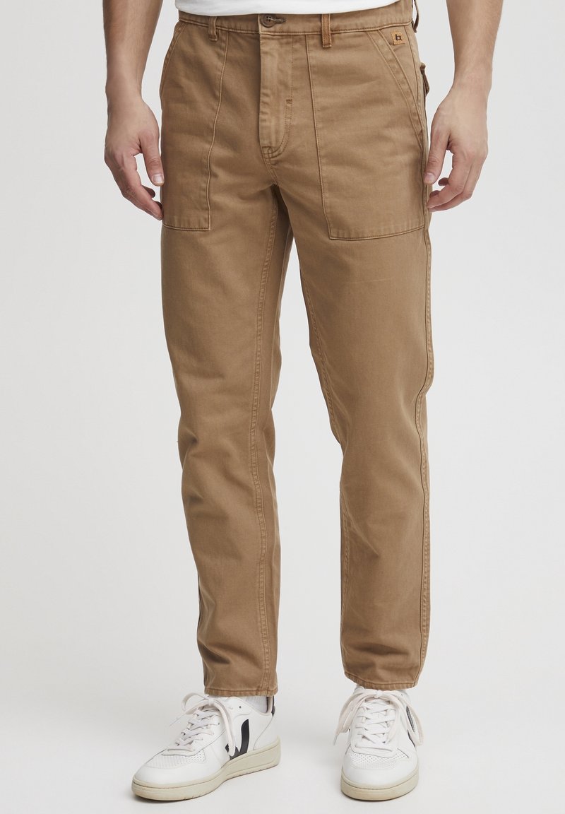 Tan katoen cargo pants met een rechte pasvorm, voorzien van twee voorzakken en een knopenvluiting. Gecombineerd met witte sneakers met zwarte accenten.